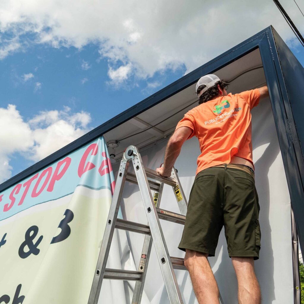 Man on ladder working on outdoor banner sign.