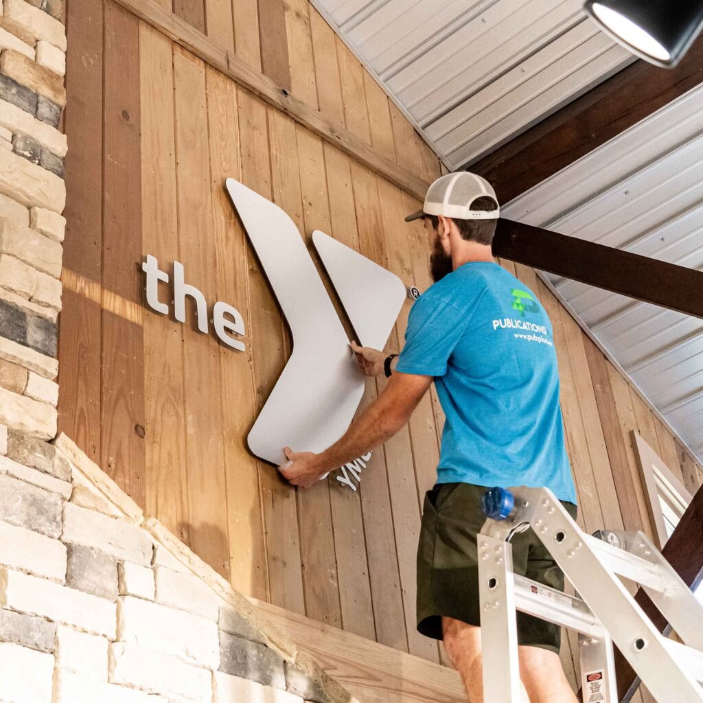 A man installing an indoor silver sign on a wooden wall.