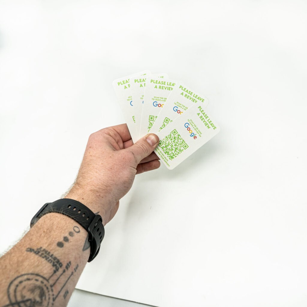 Hand holding green & white cards asking customers to leave a review.