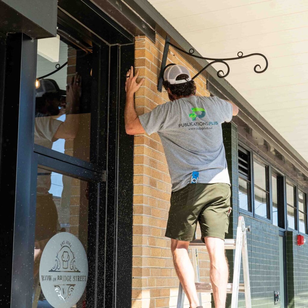 Man drilling into wall to attach a steel arm for a hanging outdoor sign.